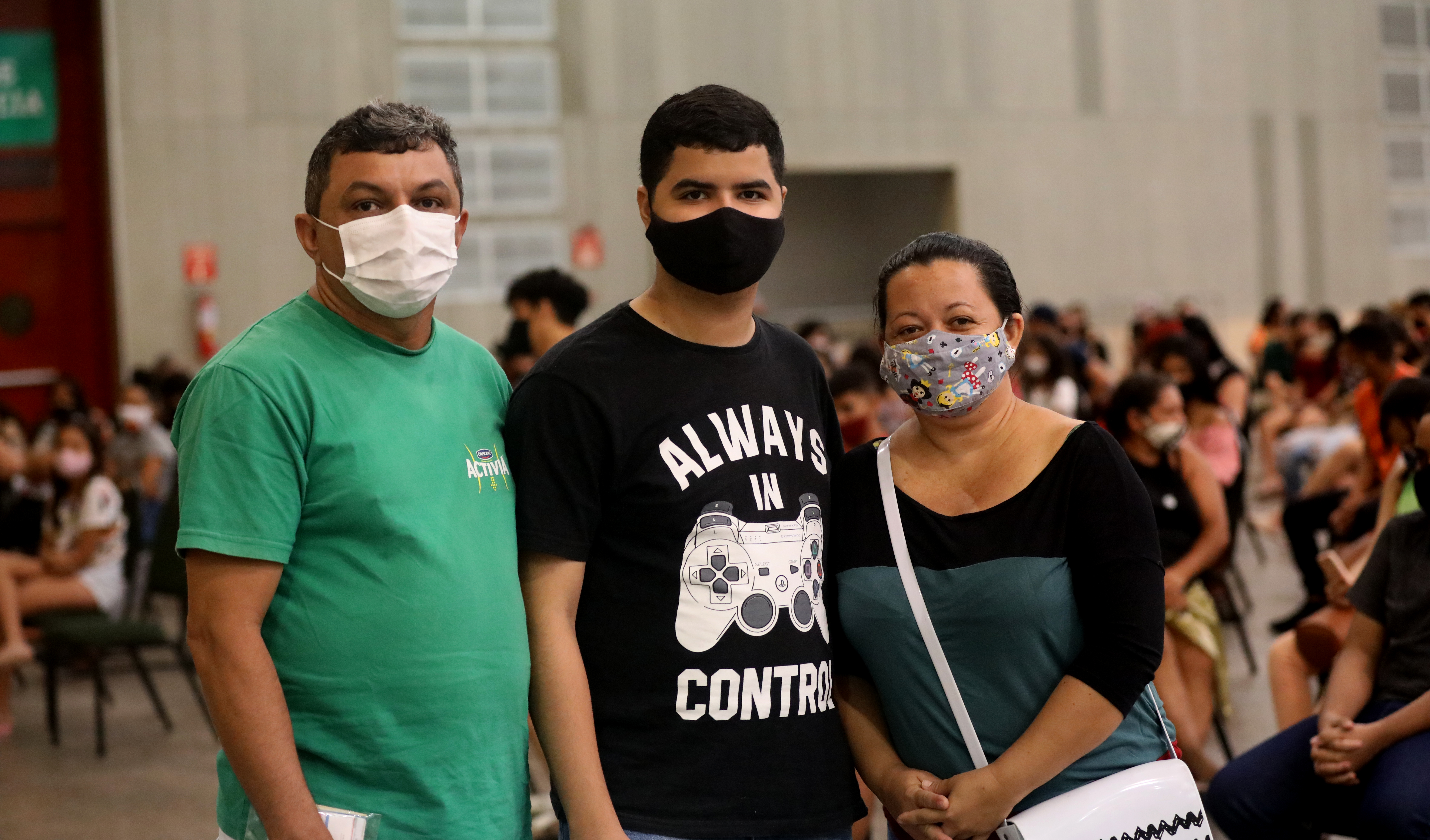 três pessoas em pé, de máscara, posam para a foto